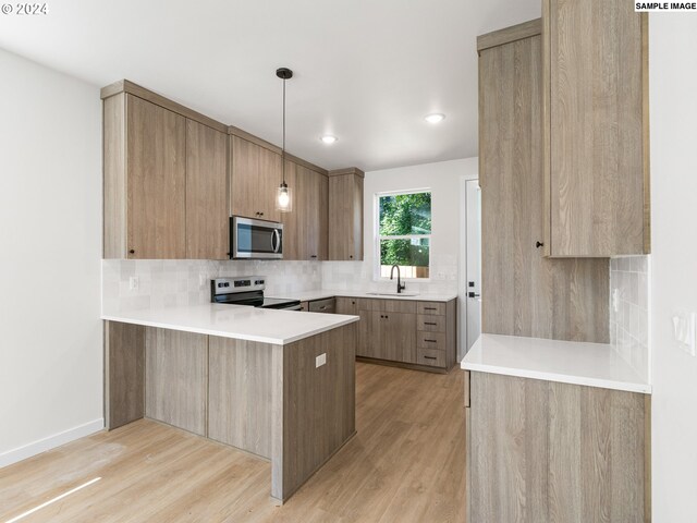 66 NE Stanton St, Portland, OR 97212 - kitchen featuring light hardwood / wood-style floors, kitchen peninsula, appliances with stainless steel finishes, hanging light fixtures, and sink