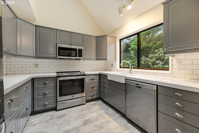 kitchen with sink, gray cabinetry, tasteful backsplash, high vaulted ceiling, and appliances with stainless steel finishes