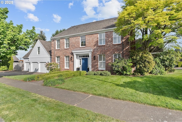 colonial-style house featuring brick siding, an attached garage, a front yard, and aphalt driveway