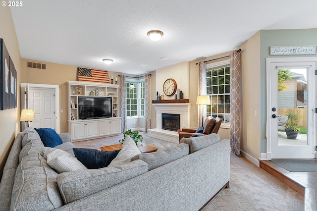 living room with visible vents, a textured ceiling, a glass covered fireplace, and a wealth of natural light