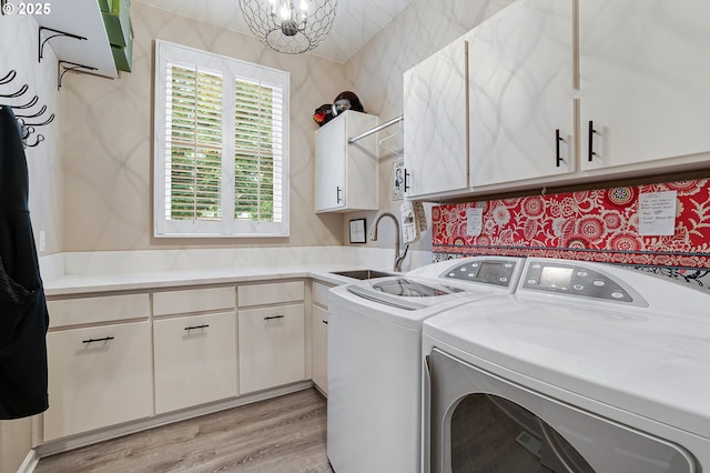 washroom with washer and dryer, cabinet space, an inviting chandelier, a sink, and light wood finished floors