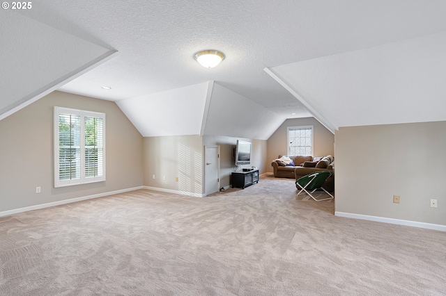 additional living space with light colored carpet, a textured ceiling, baseboards, and lofted ceiling