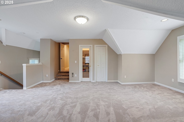 additional living space featuring carpet flooring, a textured ceiling, baseboards, and lofted ceiling