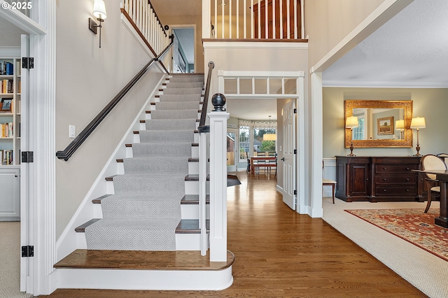 stairs featuring a high ceiling, wood finished floors, and ornamental molding