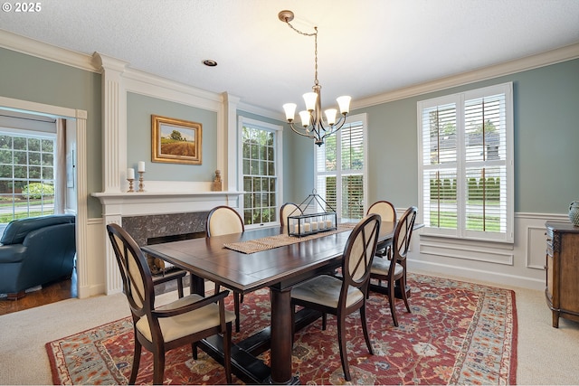 carpeted dining area with crown molding, an inviting chandelier, wainscoting, and a decorative wall