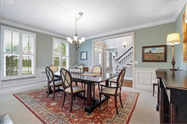 dining area with an inviting chandelier, carpet flooring, crown molding, and a wainscoted wall