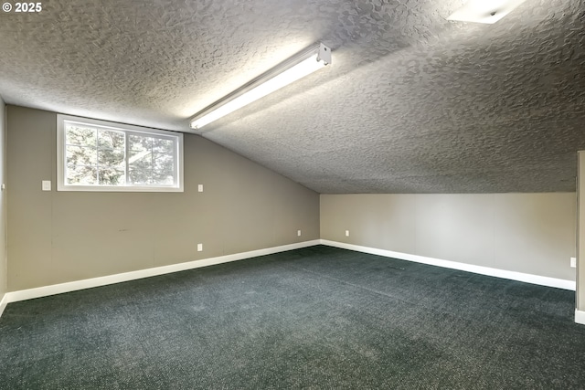additional living space featuring a textured ceiling, vaulted ceiling, baseboards, and dark colored carpet