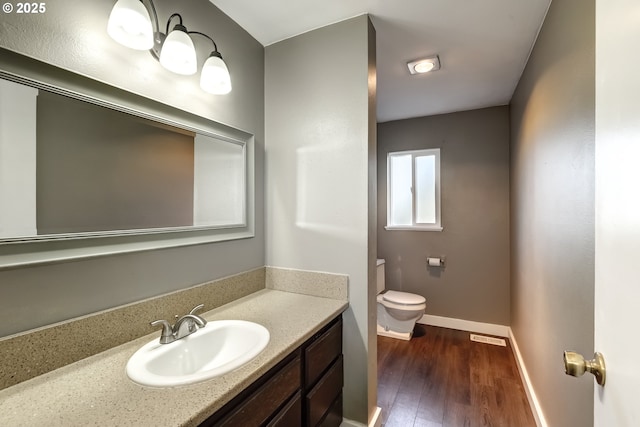 half bath with baseboards, vanity, toilet, and wood finished floors