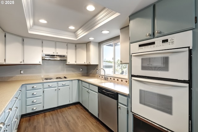 kitchen featuring dishwasher, white double oven, a sink, under cabinet range hood, and a tray ceiling
