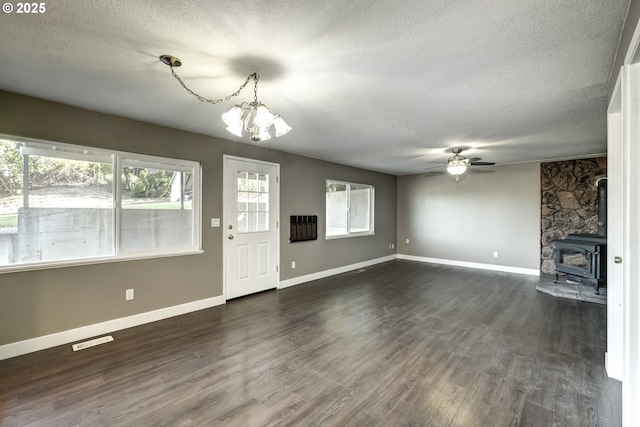 unfurnished living room with dark wood-style flooring, a textured ceiling, visible vents, a wood stove, and baseboards