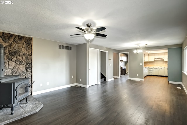 unfurnished living room with visible vents, a wood stove, baseboards, ceiling fan, and dark wood-style floors