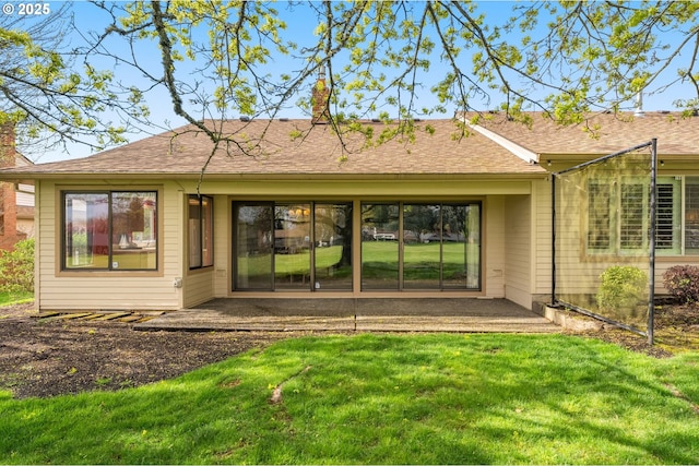 back of property featuring roof with shingles, a chimney, a patio area, and a lawn