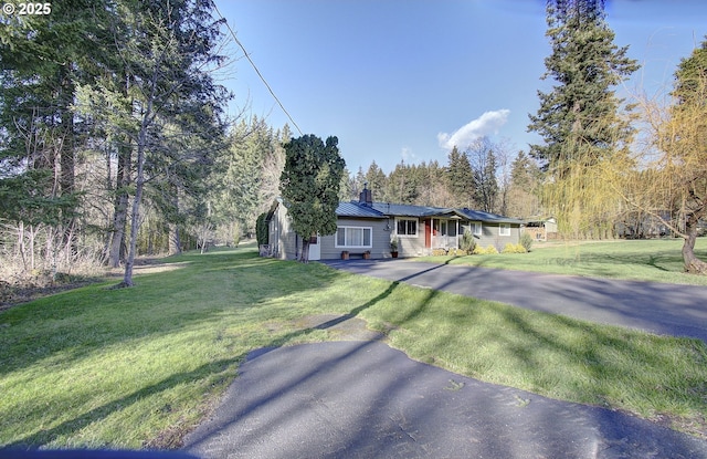 single story home featuring metal roof, a front lawn, driveway, and a standing seam roof