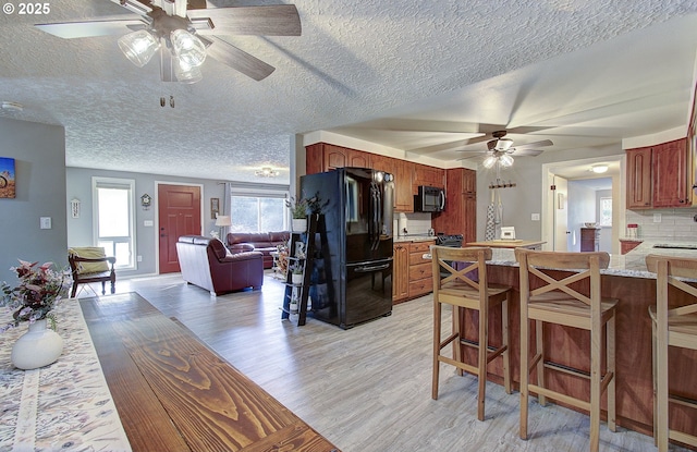 kitchen with a breakfast bar area, backsplash, black appliances, and light wood-style flooring