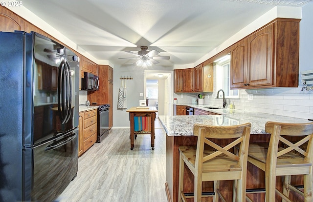 kitchen with a peninsula, ceiling fan, decorative backsplash, black appliances, and a sink