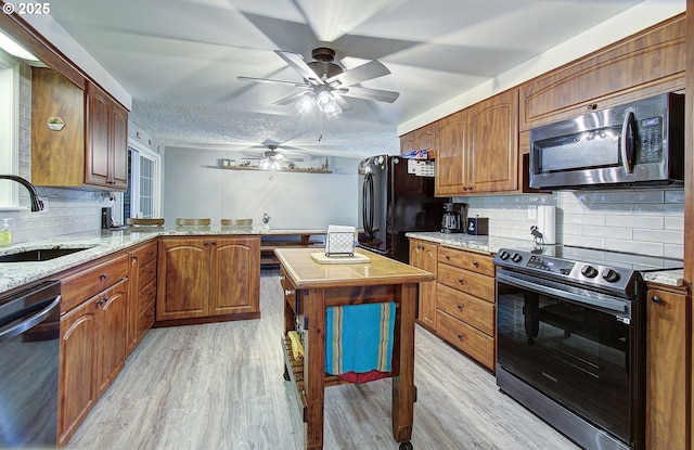 kitchen with appliances with stainless steel finishes, light wood-type flooring, a peninsula, and a sink