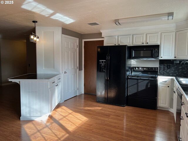 kitchen with hanging light fixtures, black appliances, light hardwood / wood-style floors, and white cabinets