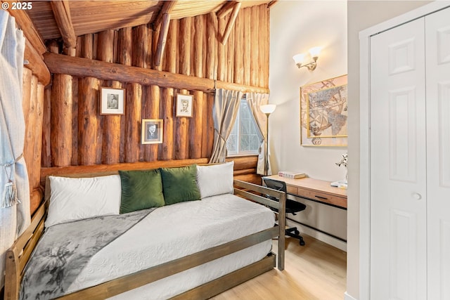 bedroom with built in desk, wooden walls, lofted ceiling with beams, wooden ceiling, and light wood-type flooring