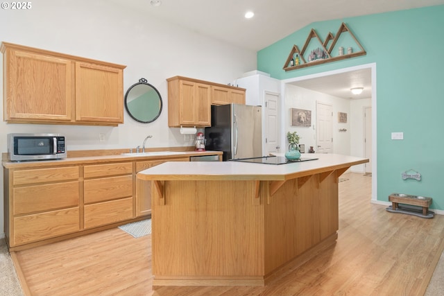 kitchen with a sink, a kitchen breakfast bar, a kitchen island, appliances with stainless steel finishes, and light countertops