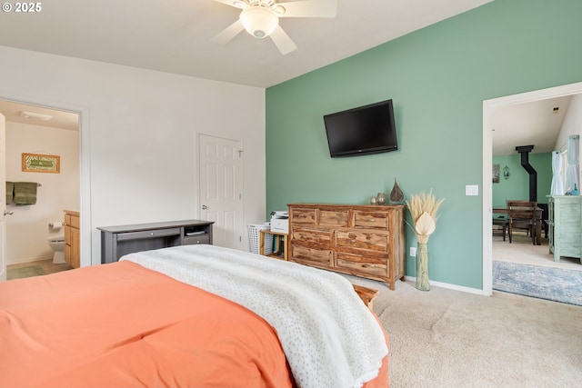 carpeted bedroom with ensuite bath, a wood stove, baseboards, and ceiling fan