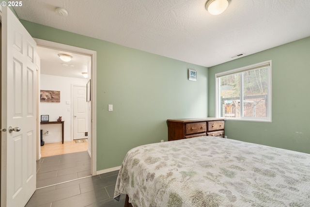 bedroom featuring visible vents, a textured ceiling, baseboards, and dark tile patterned flooring