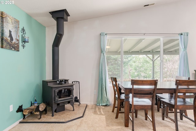 carpeted dining space featuring visible vents, baseboards, and a wood stove