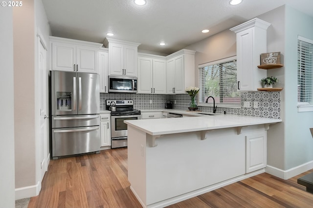 kitchen with stainless steel appliances, a peninsula, light wood-style flooring, and a sink