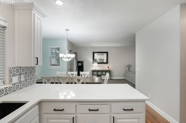 kitchen with light stone counters, a chandelier, a peninsula, a textured ceiling, and white cabinets