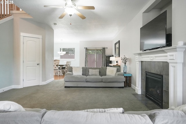 living room with dark colored carpet, baseboards, a fireplace, a textured ceiling, and ceiling fan with notable chandelier