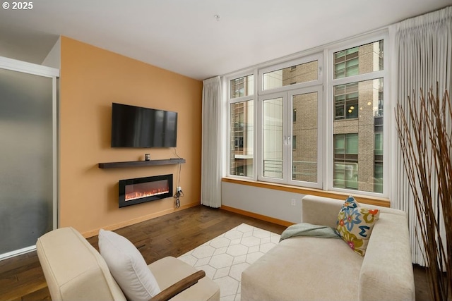 living room featuring a glass covered fireplace, baseboards, and wood finished floors