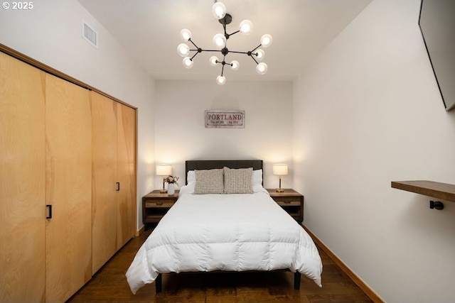 bedroom with baseboards, visible vents, dark wood-type flooring, a chandelier, and a closet