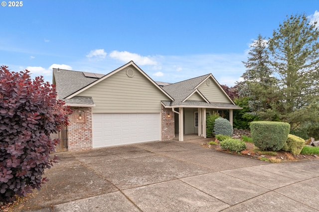 15745 SE Bybee Dr, Portland, OR 97236 - view of front of house with driveway, an attached garage, brick siding, solar panels, and roof with shingles