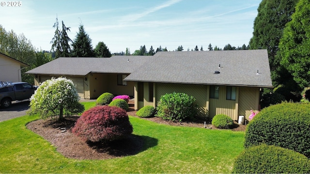 ranch-style house featuring an attached garage, a front lawn, and roof with shingles