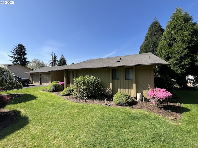 rear view of property with an attached garage, a yard, and driveway