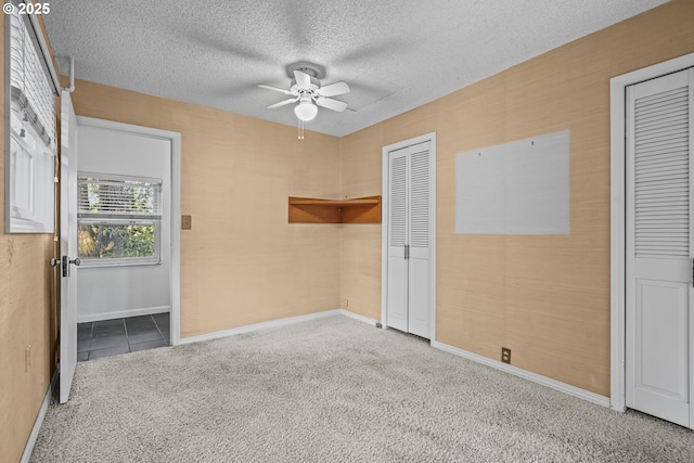 unfurnished bedroom featuring multiple closets, ceiling fan, a textured ceiling, and carpet