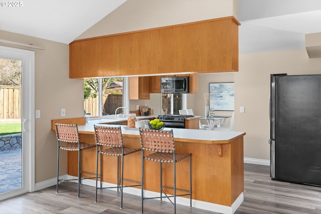 kitchen with light countertops, lofted ceiling, a peninsula, wood finished floors, and stainless steel appliances