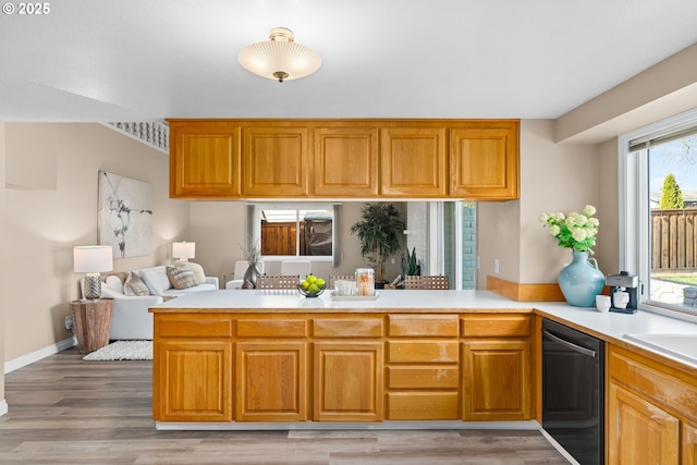 kitchen featuring a peninsula, light countertops, light wood-style floors, dishwasher, and open floor plan