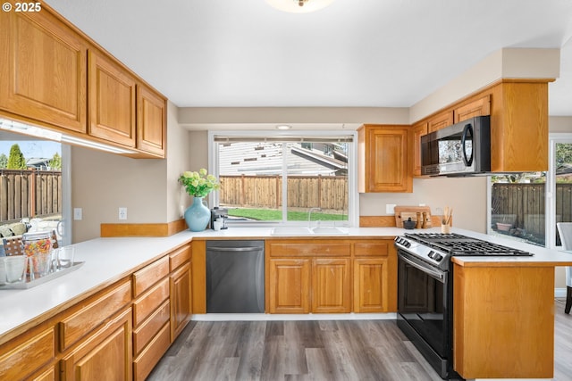 kitchen featuring gas range, light countertops, dishwashing machine, a peninsula, and a sink