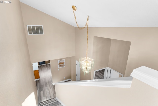 stairway with visible vents, a notable chandelier, wood finished floors, and vaulted ceiling