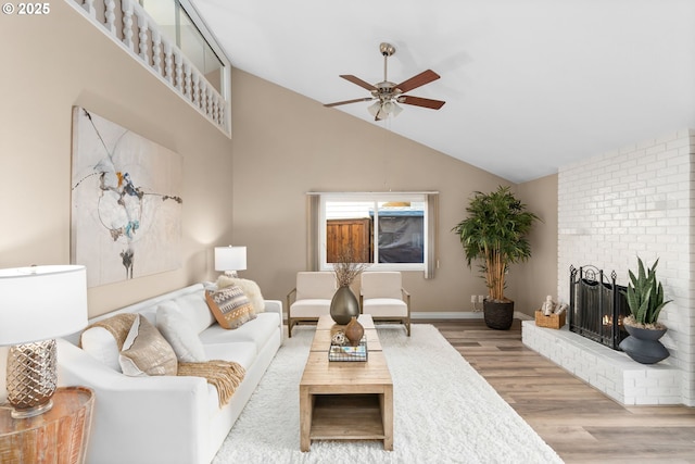 living area with a brick fireplace, baseboards, light wood-style flooring, high vaulted ceiling, and a ceiling fan