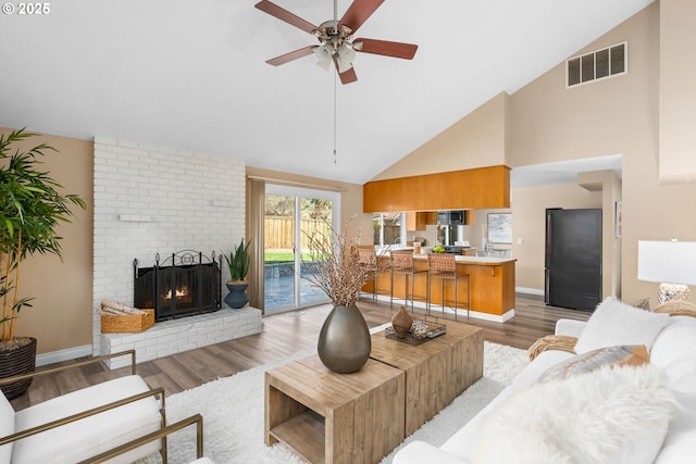 living room with visible vents, light wood-style flooring, a fireplace, baseboards, and ceiling fan