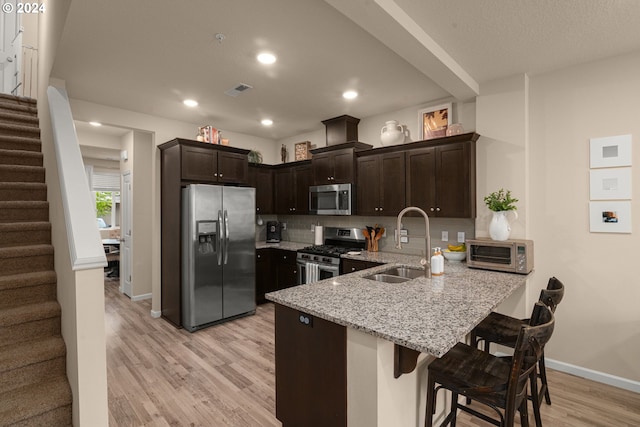 kitchen with kitchen peninsula, a breakfast bar, dark brown cabinets, stainless steel appliances, and sink