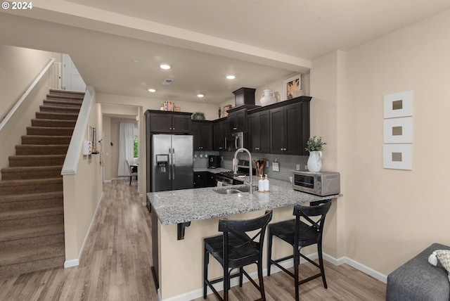 kitchen featuring light stone counters, backsplash, kitchen peninsula, light hardwood / wood-style floors, and appliances with stainless steel finishes