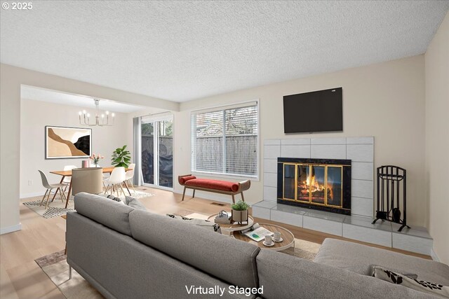 living room with baseboards, a chandelier, a tiled fireplace, a textured ceiling, and wood finished floors