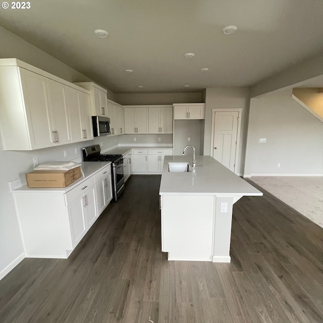 kitchen with dark wood-style floors, appliances with stainless steel finishes, a kitchen island with sink, white cabinets, and a sink