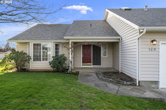 view of exterior entry featuring a garage, a lawn, and a shingled roof