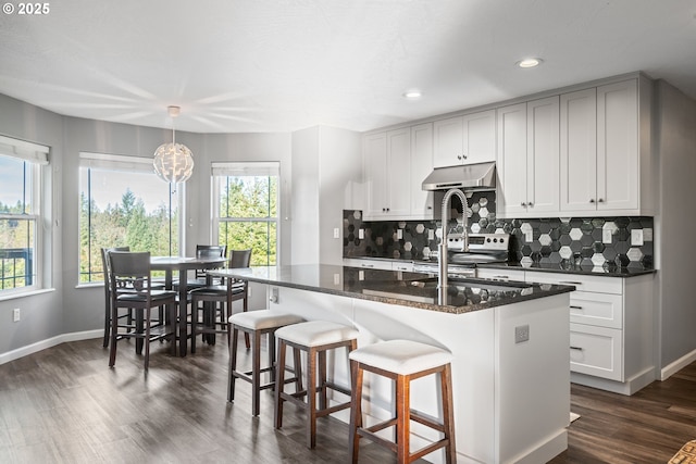 kitchen featuring decorative light fixtures, decorative backsplash, a center island with sink, and dark stone countertops