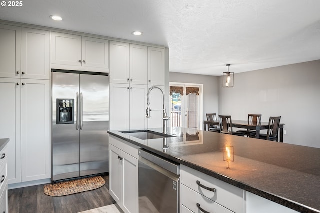 kitchen with appliances with stainless steel finishes, dark hardwood / wood-style flooring, a textured ceiling, pendant lighting, and sink