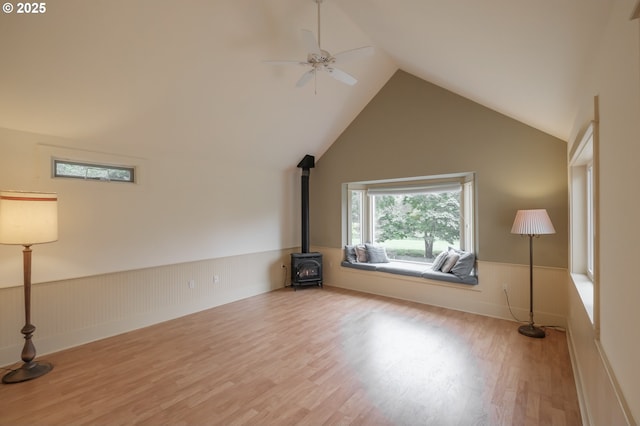unfurnished room with a wood stove, a wainscoted wall, wood finished floors, lofted ceiling, and ceiling fan