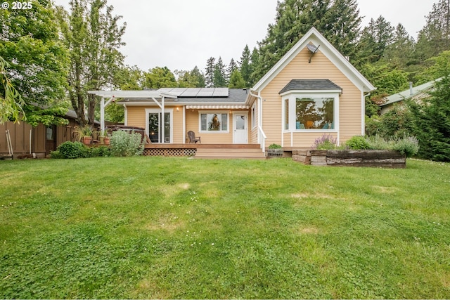 rear view of house featuring solar panels, a deck, and a yard